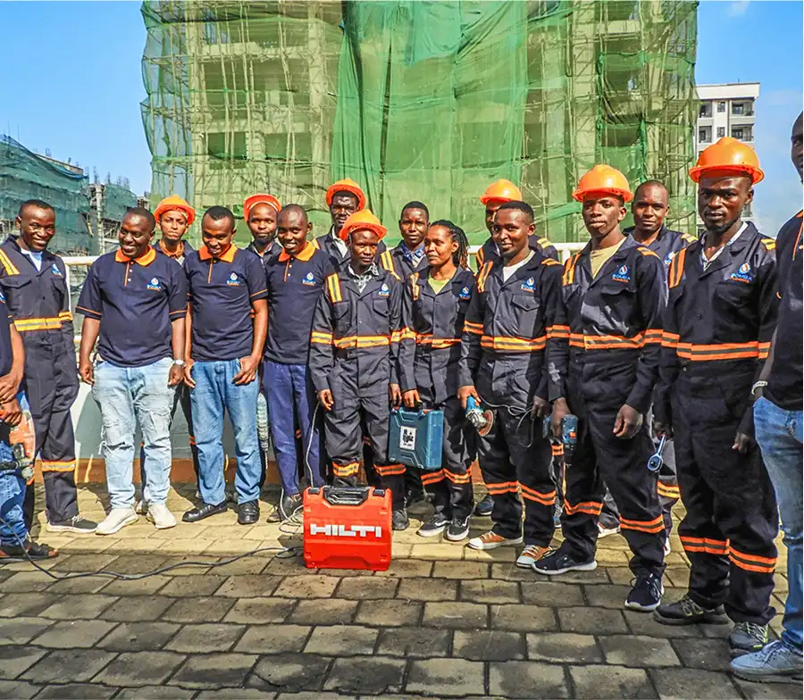 Group photo of Bomba Plumbers technicians in uniforms and hard hats at a construction site .