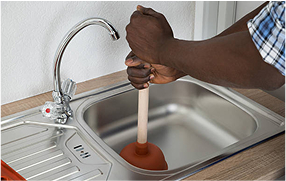Hand using a plunger on a kitchen sink drain – Bomba Plumbers drain unclogging service.