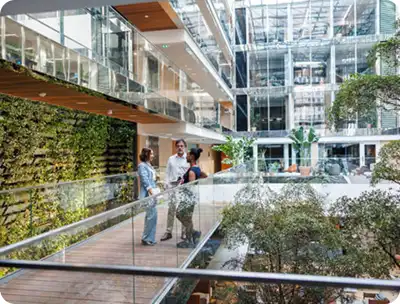 Modern office atrium with glass walls and indoor greenery where people are conversing – representing Bomba Plumbers’ commercial clients.